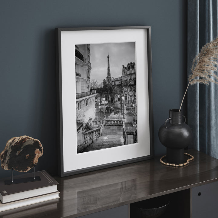 a framed black and white photograph of the Eiffel Tower in Paris, France, displayed on a wooden surface.