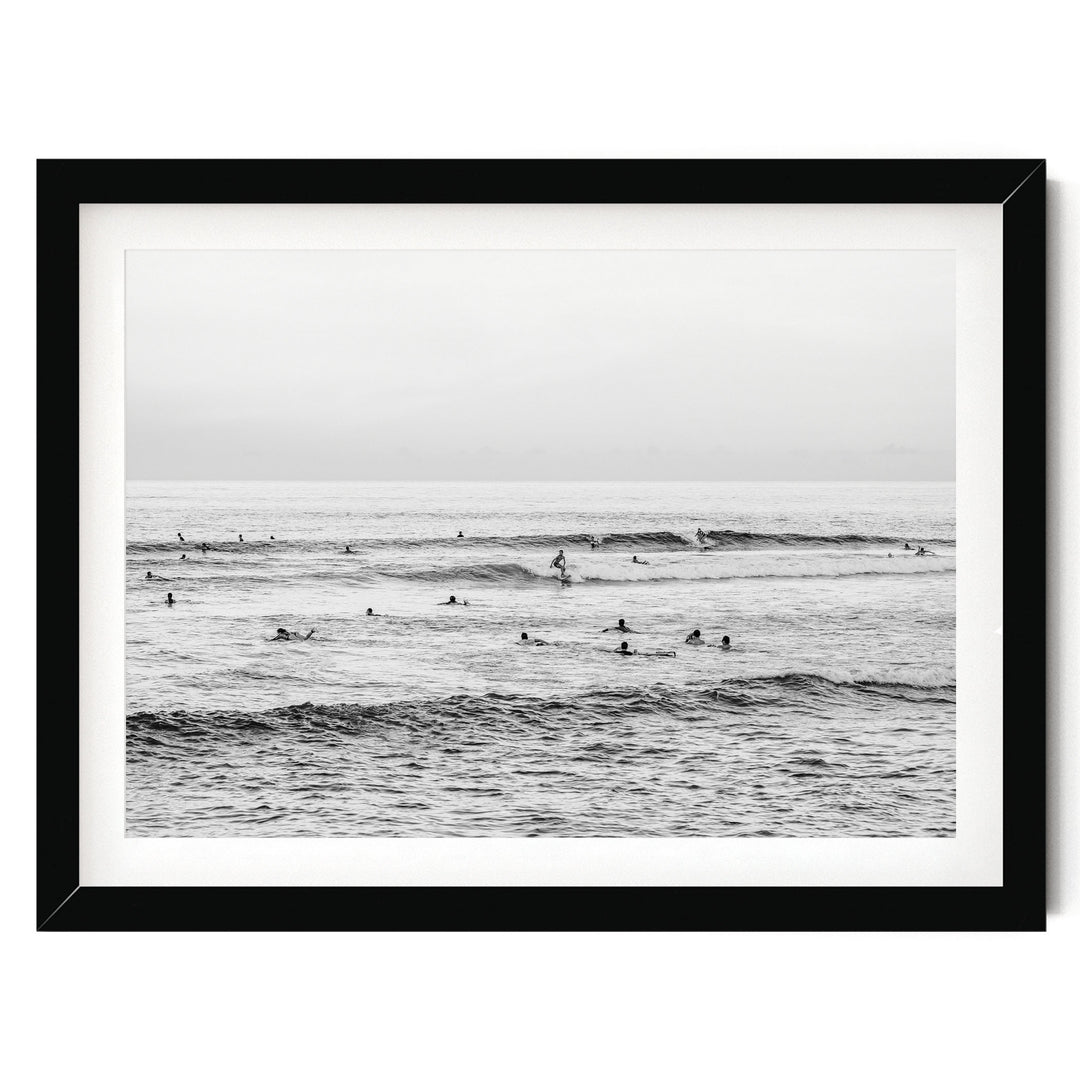 A black and white photograph of a group of people surfing in the ocean, with waves visible in the background.