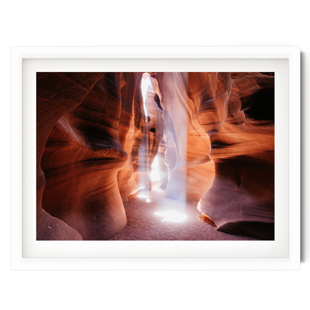 A framed photograph depicting a narrow, winding path through a canyon with a bright light shining through the rock formations.