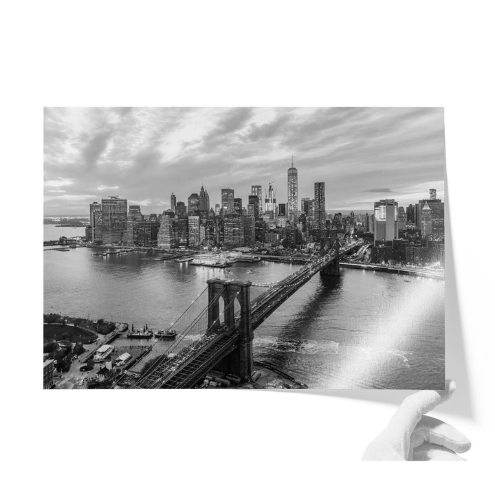 A black and white photograph of the New York City skyline, featuring the Brooklyn Bridge and the surrounding cityscape.
