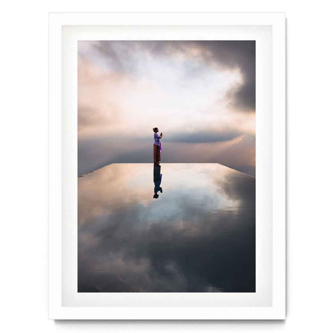 A person stands on a reflective surface, gazing out at the cloudy sky, creating a serene and contemplative scene.