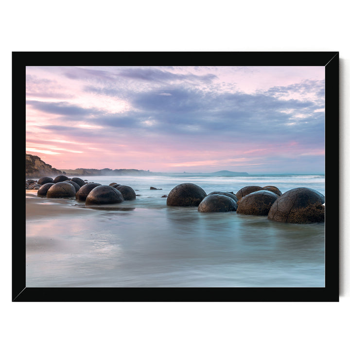 A serene beach scene with a collection of large, round boulders in the water, set against a backdrop of a colorful sunset sky.