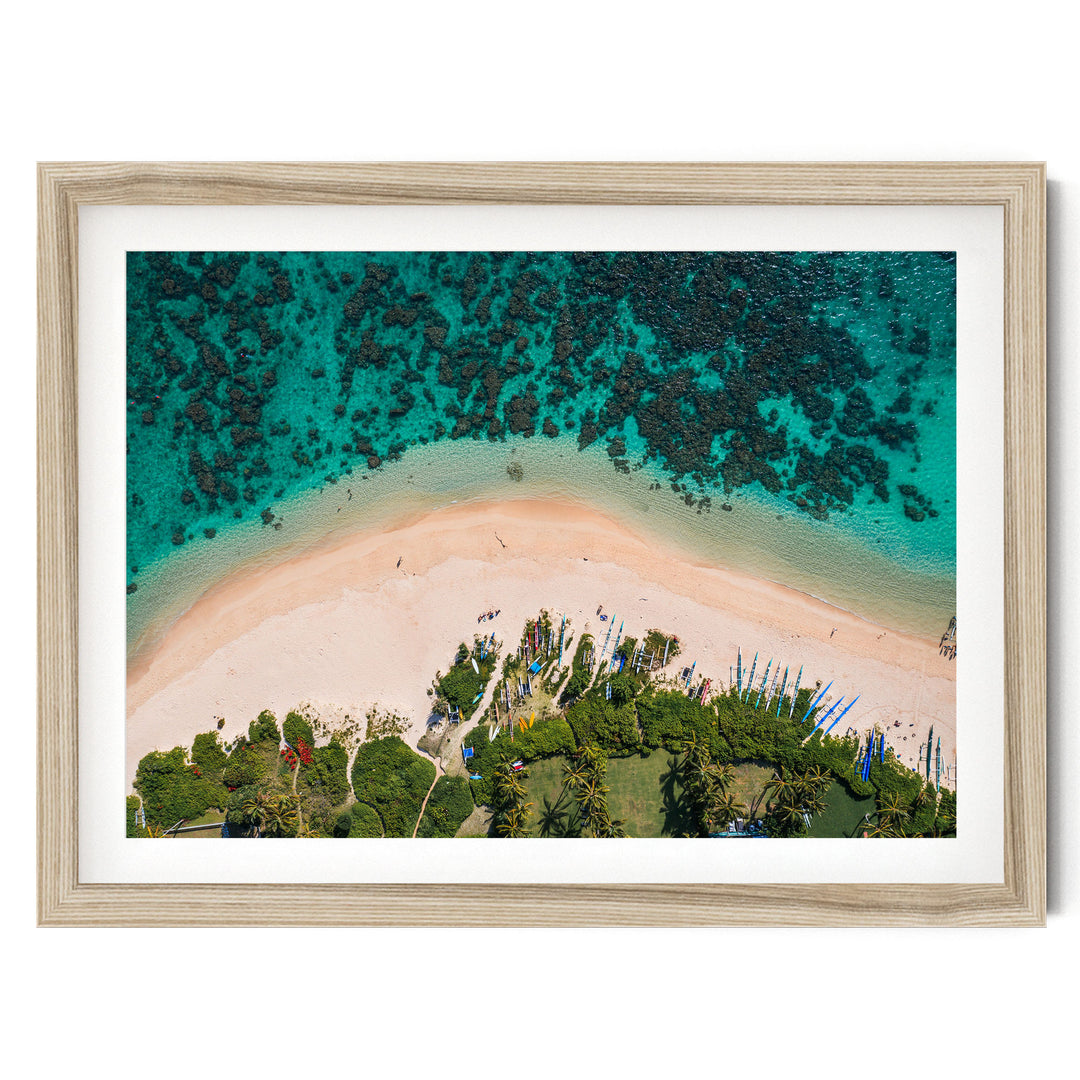 The image is an aerial view of a tropical beach with a sandy shore, lush vegetation, and a clear turquoise ocean.