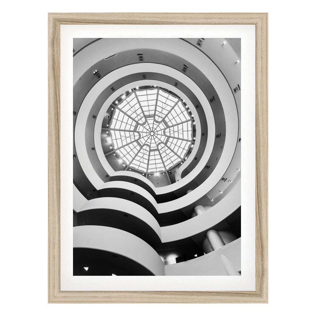 A black and white photograph of a spiral staircase with a large circular skylight at the top, creating a striking visual effect.