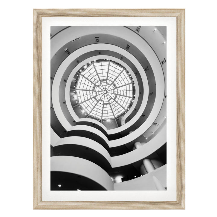 A black and white photograph of a spiral staircase with a large circular skylight at the top, creating a striking visual effect.