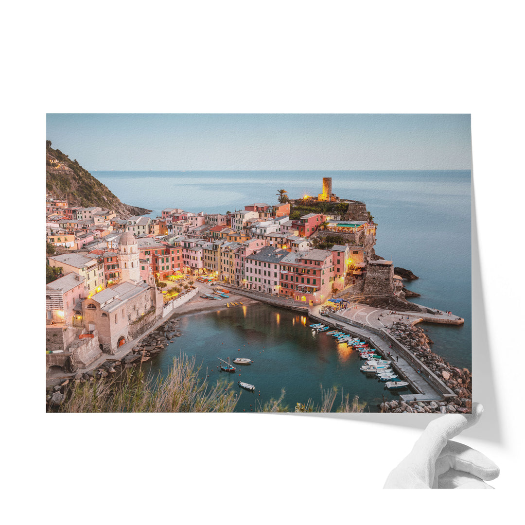 A picturesque coastal town with colorful buildings, a lighthouse on a cliff, and boats in the harbor, all illuminated at night.