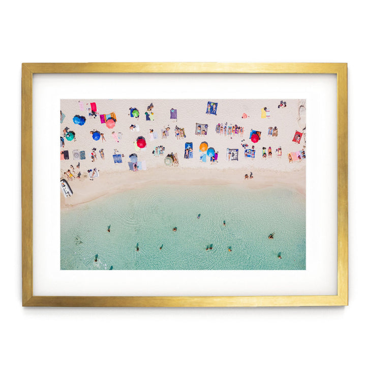The image is a framed photograph depicting a beach scene with people relaxing on the sand and in the water.