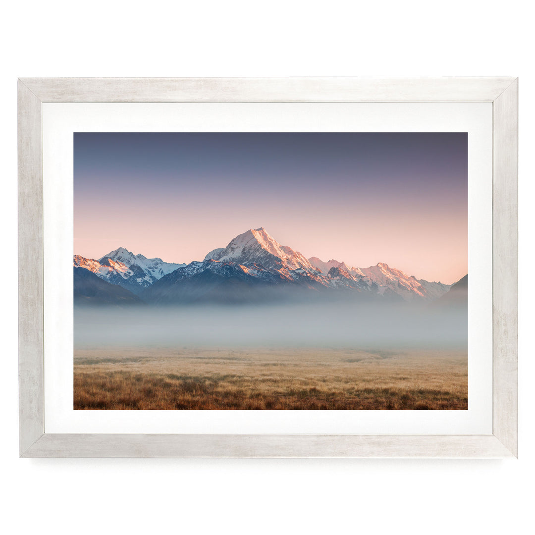 A breathtaking landscape featuring a majestic mountain range with snow-capped peaks, set against a vibrant sky at sunset. The foreground is a vast expanse of golden grass, creating a striking contrast with the natural scenery.