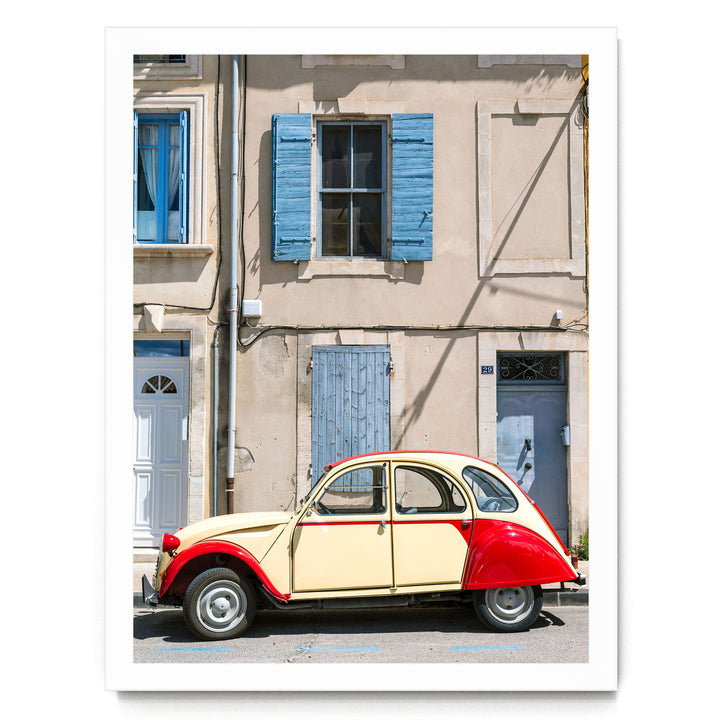 A vintage yellow and red car is parked on a street in front of a building with blue shutters and a white door.