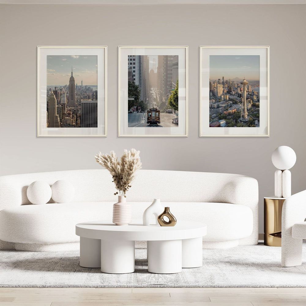 a modern living room with a white sofa, a round coffee table, and three framed cityscape photographs hanging on the wall above the sofa.
