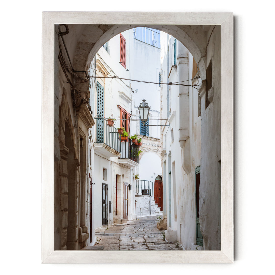 a narrow, cobblestone street lined with white buildings featuring colorful shutters and balconies.