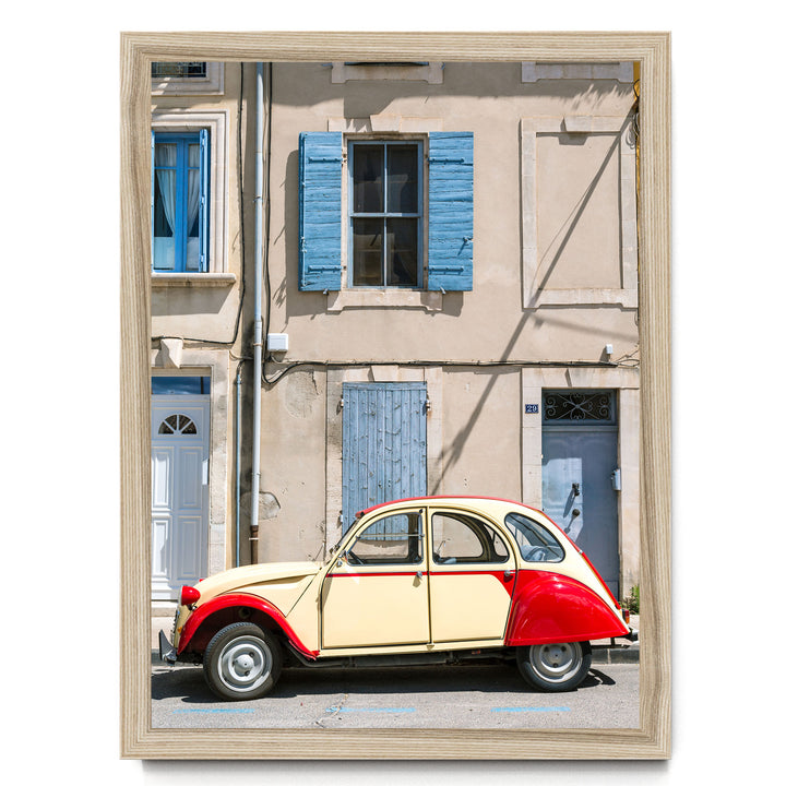 A vintage red and cream-colored car is parked in front of a building with blue shutters and a white door.