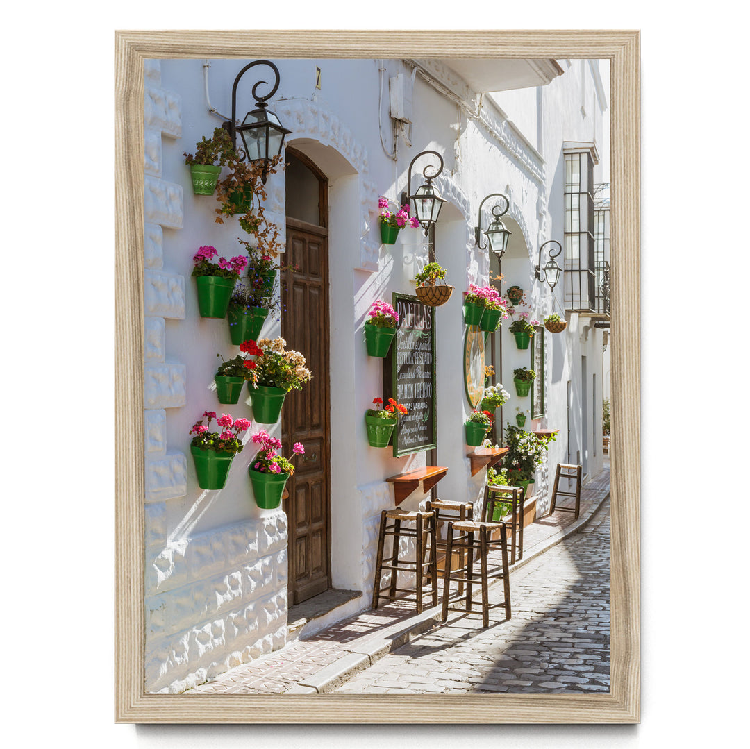 A charming street scene with white buildings, green planters, and wooden furniture, creating a cozy and inviting atmosphere.