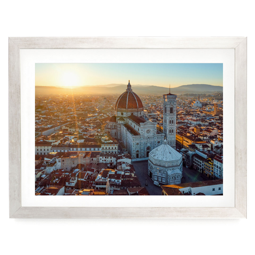 a cityscape with a large domed building, possibly a church or cathedral, surrounded by smaller buildings and structures. The sun is setting, casting a warm glow over the scene and creating a picturesque view of the city.
