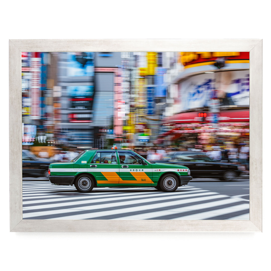 A green taxi cab is driving through a busy city street with tall buildings and colorful signs in the background.