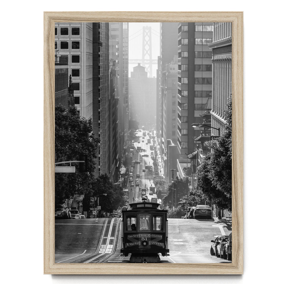 A black and white photograph of a trolley car traveling down a busy city street, with tall buildings and a bridge visible in the background.