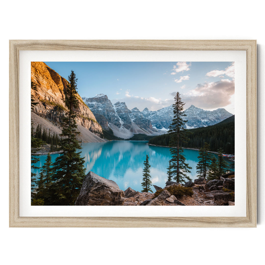 A framed photograph depicting a serene mountain landscape with a deep blue lake surrounded by snow-capped peaks and pine trees.
