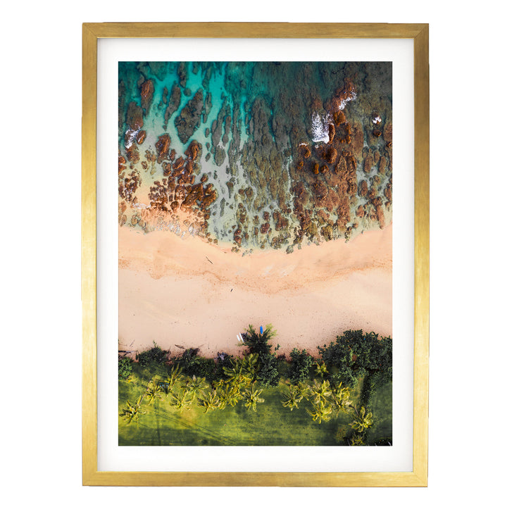 The image is a framed aerial view of a beach with a mix of green vegetation, sandy beach, and rocky formations.