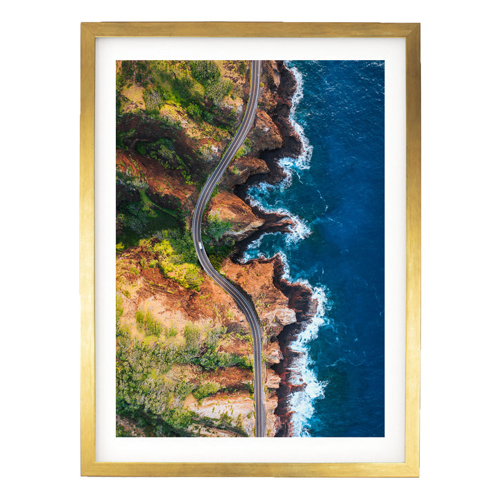 The image is an aerial view of a winding road cutting through a rugged coastline with cliffs and the ocean.