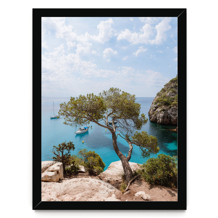 A scenic view of a rocky coastline with a large tree, a small boat, and a larger boat in the distance, all set against a backdrop of a clear blue sky with fluffy white clouds.
