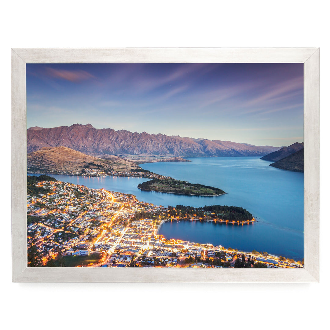 a picturesque town nestled at the foot of a mountain range, with the town's lights twinkling in the evening and the surrounding mountains bathed in a warm, golden glow.