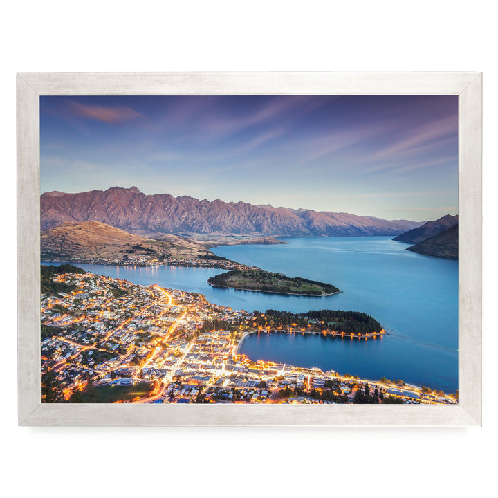 a picturesque town nestled at the foot of a mountain range, with the town's lights twinkling in the evening and the surrounding mountains bathed in a warm, golden glow.