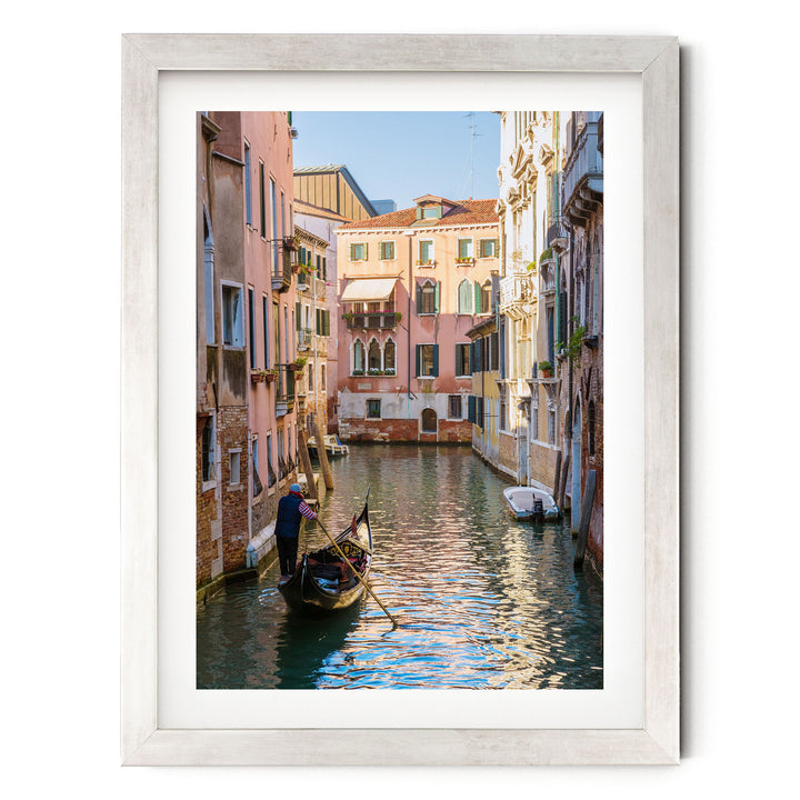 A gondola glides through a picturesque canal in Venice, Italy, surrounded by colorful buildings and reflecting the clear blue sky.