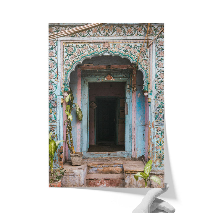 a colorful, ornately decorated doorway with a wooden frame and a small arch above it. The doorway is surrounded by lush greenery, including potted plants and a tree. The overall scene is vibrant and visually appealing.