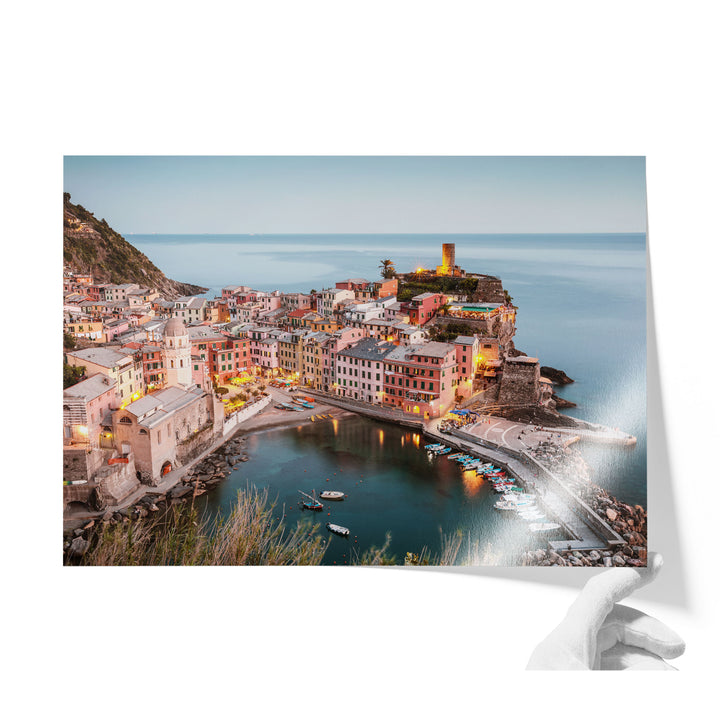 A picturesque coastal town with colorful buildings, a lighthouse on a cliff, and boats in the harbor, all illuminated at night.