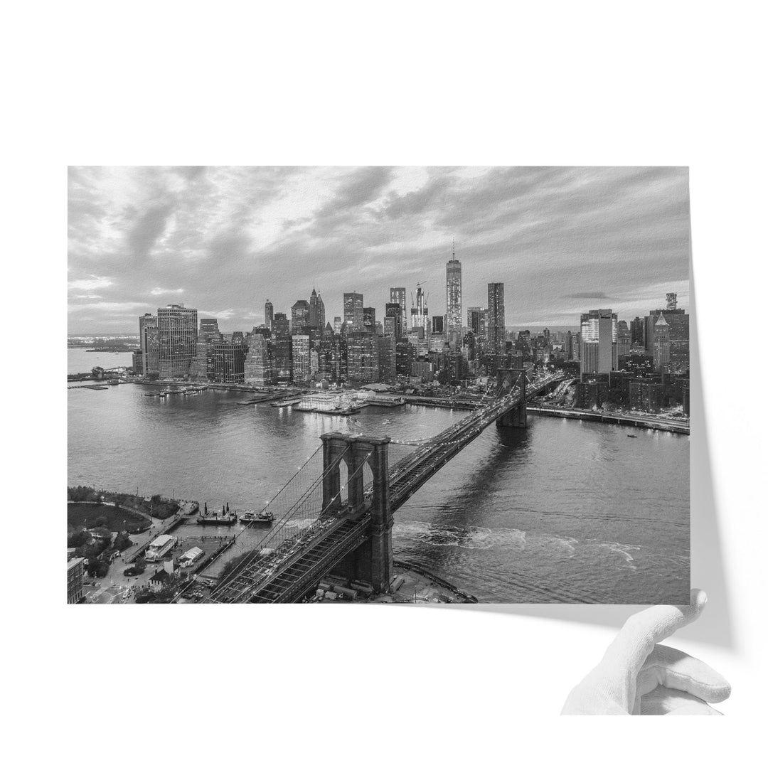 A black and white photograph of the New York City skyline, featuring the Brooklyn Bridge and the surrounding cityscape.
