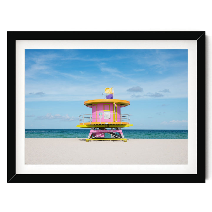 A lifeguard tower painted in vibrant pink and yellow stands on a sandy beach, overlooking the ocean.
