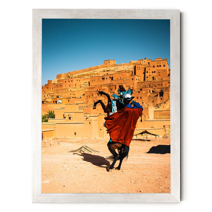 A person riding a horse in a desert-like setting, with a large, multi-story structure in the background.