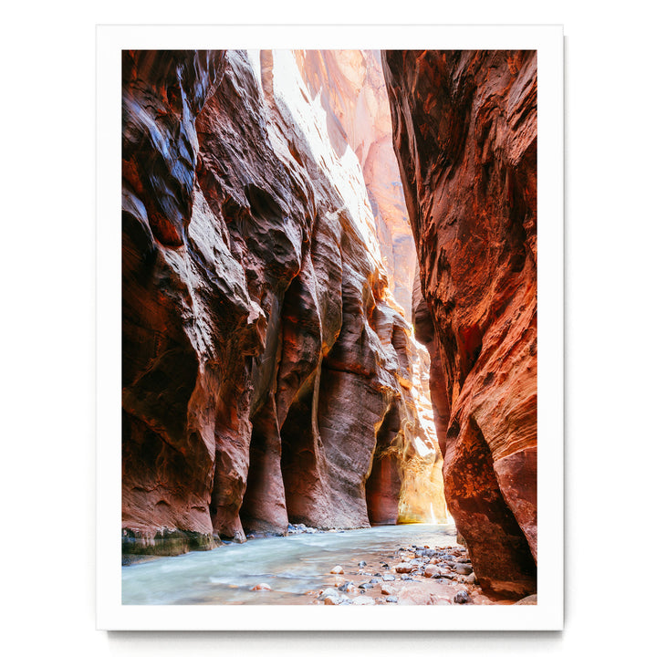 A narrow, winding river flows through a canyon with towering red rock walls on either side.