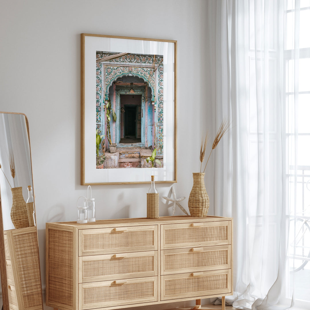 a wooden dresser with a mirror and a framed picture of an ornate doorway on the wall above it.