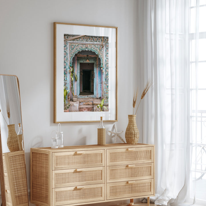 a wooden dresser with a mirror and a framed picture of an ornate doorway on the wall above it.