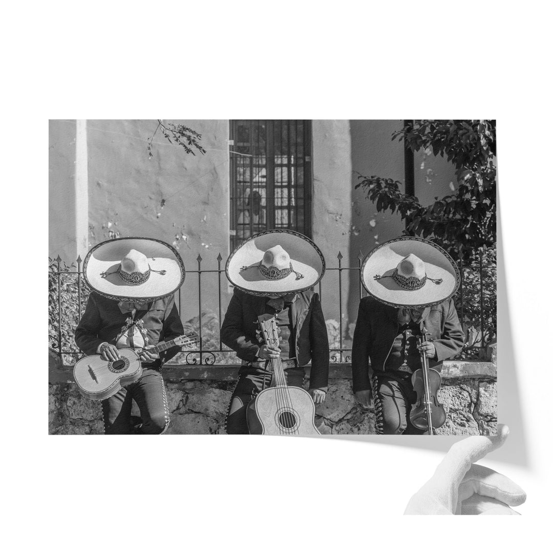 Three musicians wearing sombreros and playing instruments, including guitars and drums, in front of a building.
