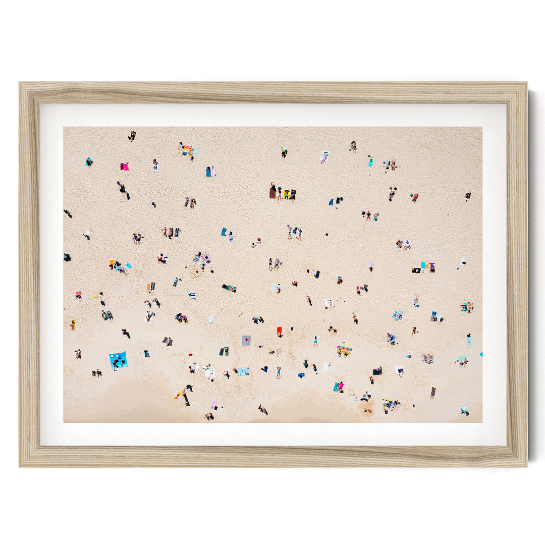 The image is a framed photograph depicting a beach scene with numerous people scattered across the sandy surface.