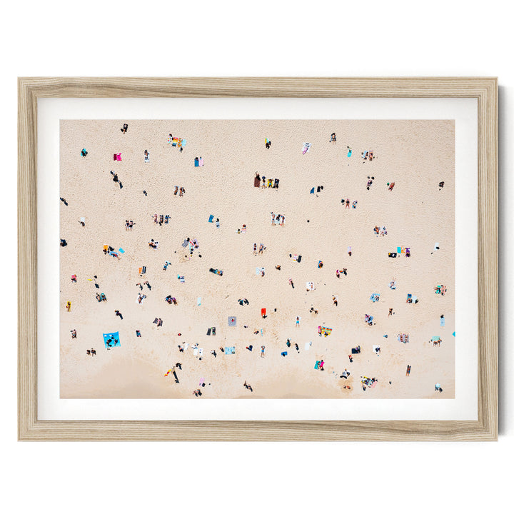The image is a framed photograph depicting a beach scene with numerous people scattered across the sandy surface.