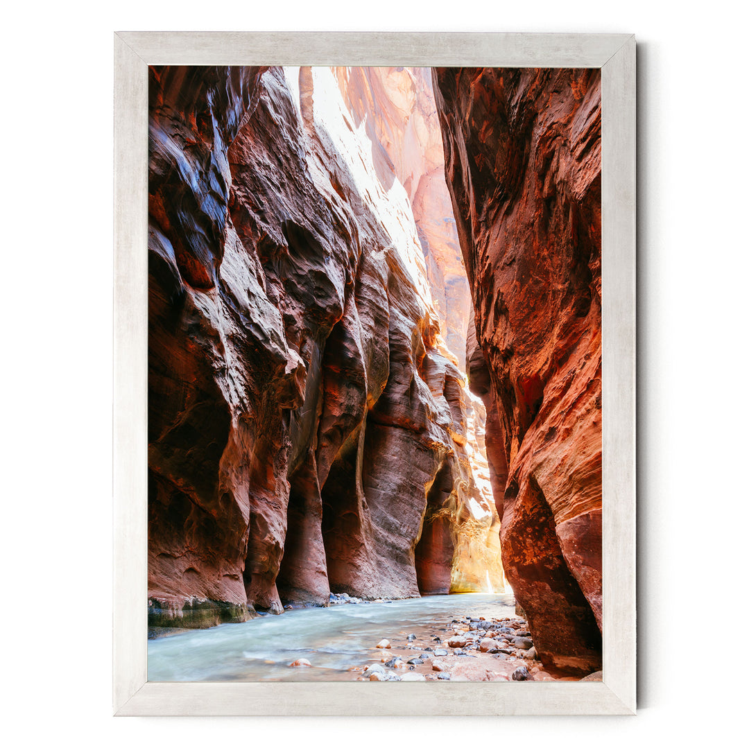 A framed photograph depicting a narrow, winding river flowing through a canyon with towering red rock walls on either side.