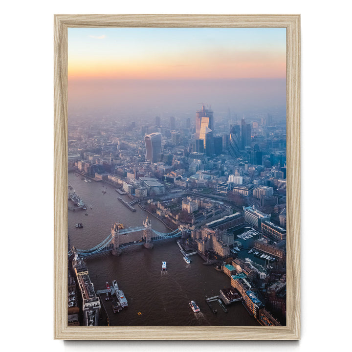 The image is an aerial view of a cityscape with a river running through it, featuring a bridge and boats on the water. The city is densely populated with tall buildings, and the sky is filled with warm, hazy colors, suggesting a sunrise or sunset.