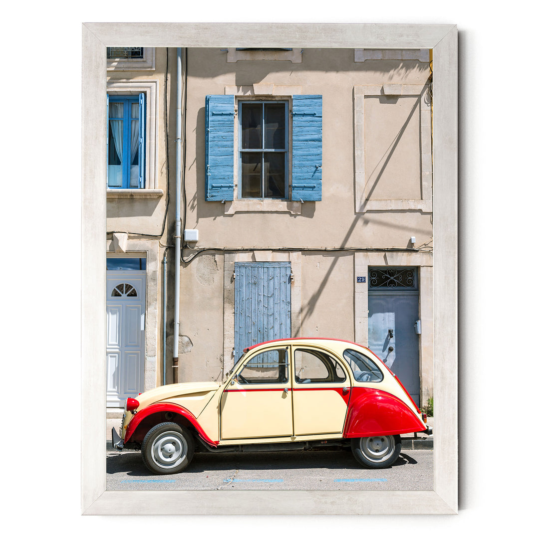 A vintage car is parked in front of a building with blue shutters and a white door.