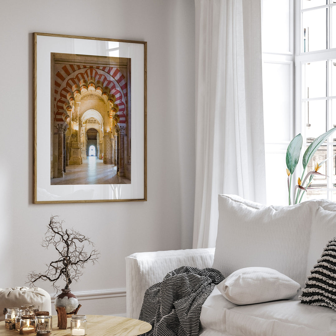 a living room with a white sofa, a framed picture of an archway, and a vase with a plant on a coffee table.