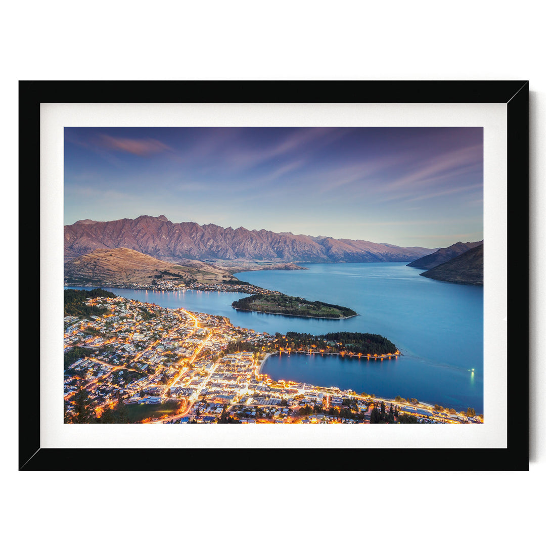A picturesque view of a coastal town at sunset, with the town's lights illuminating the landscape and the surrounding mountains in the background.