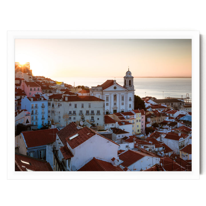 a picturesque town with a church and colorful buildings set against a backdrop of a sunset over the ocean.