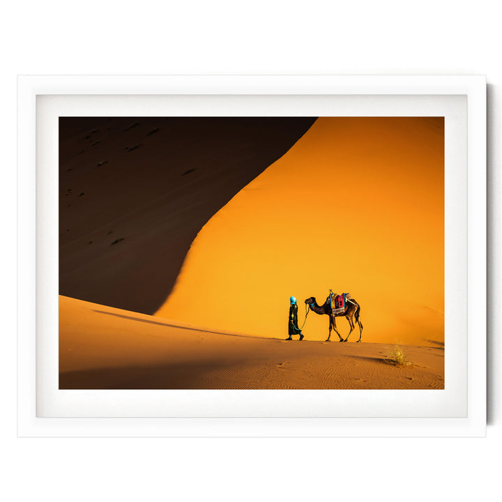 A person is walking a camel across a desert landscape with a large sand dune in the background.