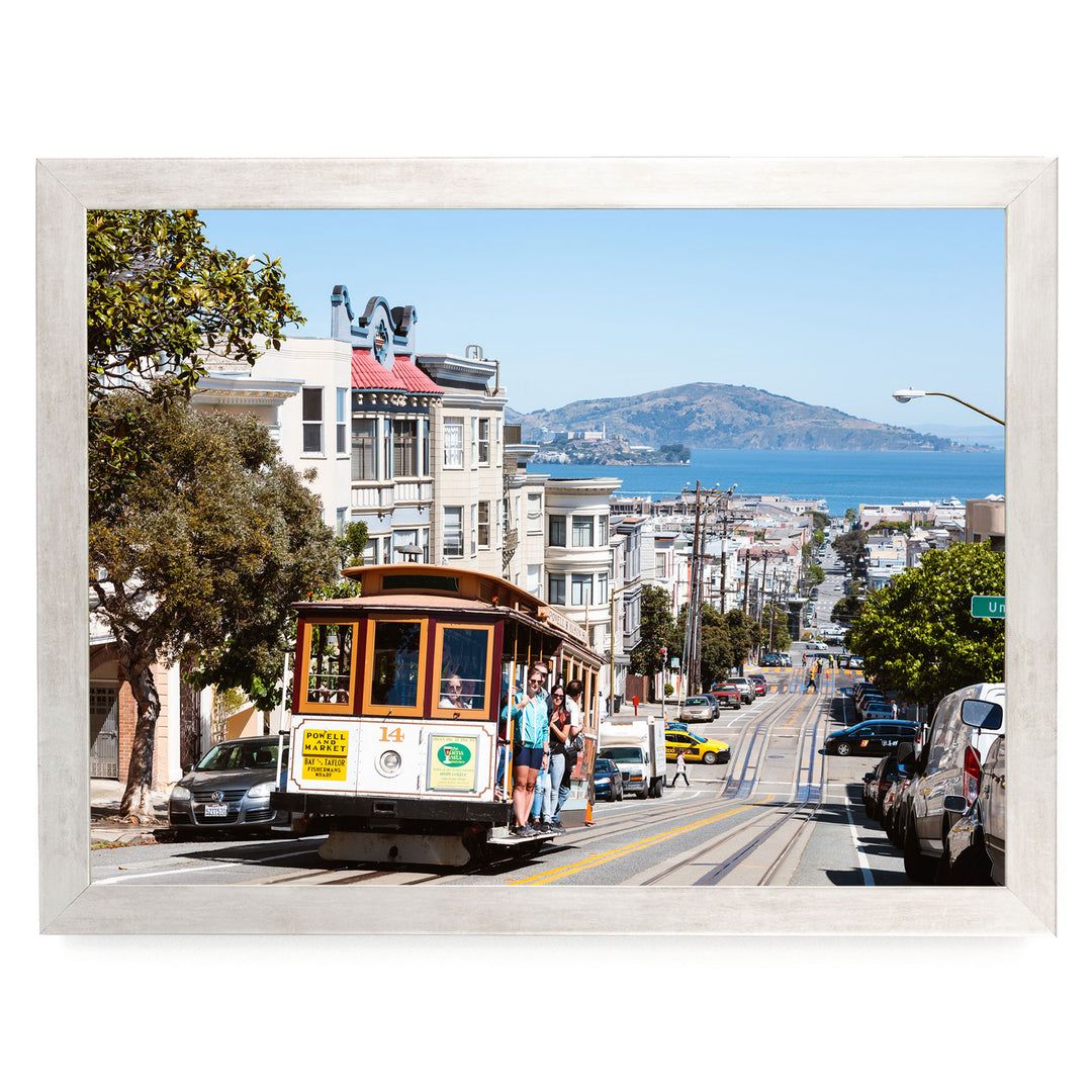 A cable car is traveling down a busy street in San Francisco, with buildings, cars, and pedestrians visible in the background.
