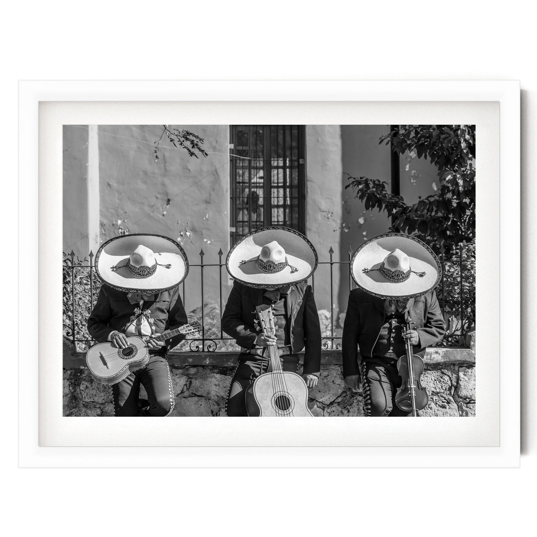 Three musicians wearing sombreros and playing guitar and drums in a row, with a stone wall and window in the background.