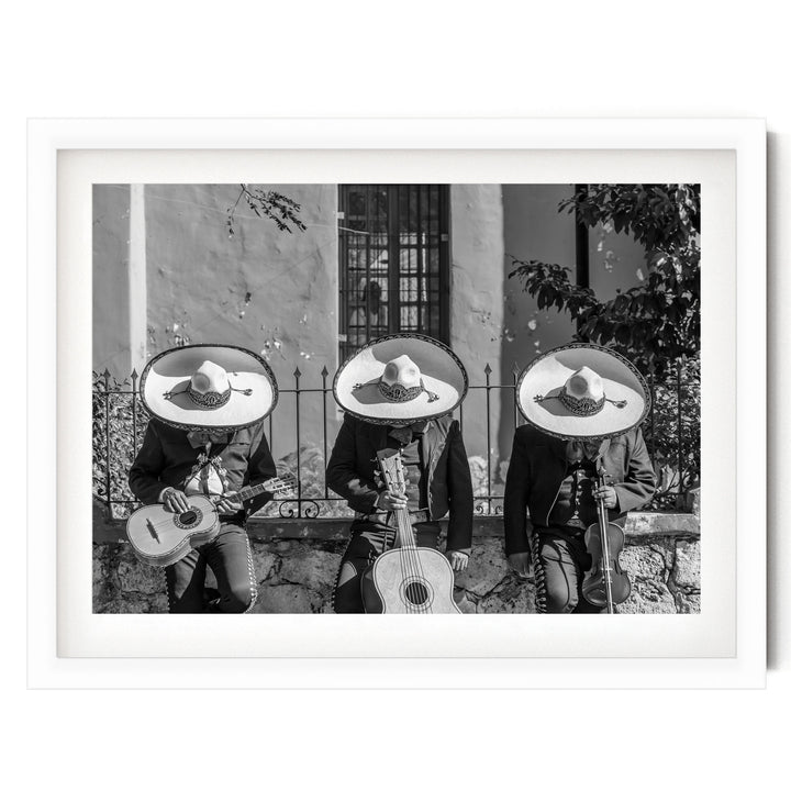 Three musicians wearing sombreros and playing guitar and drums in a row, with a stone wall and window in the background.