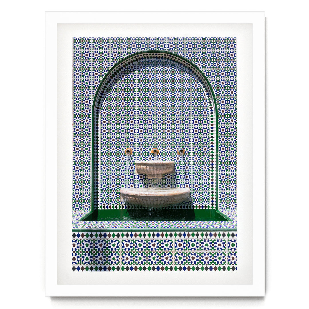 a white fountain with a green border, set against a background of a repeating pattern of blue and white tiles.