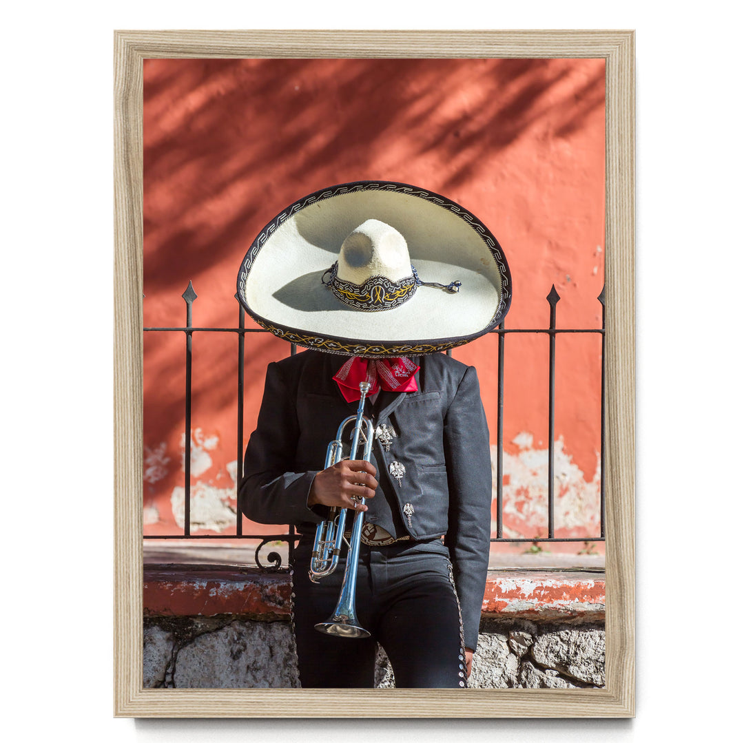 A person wearing a sombrero and a black jacket is playing a trumpet in front of a red wall.